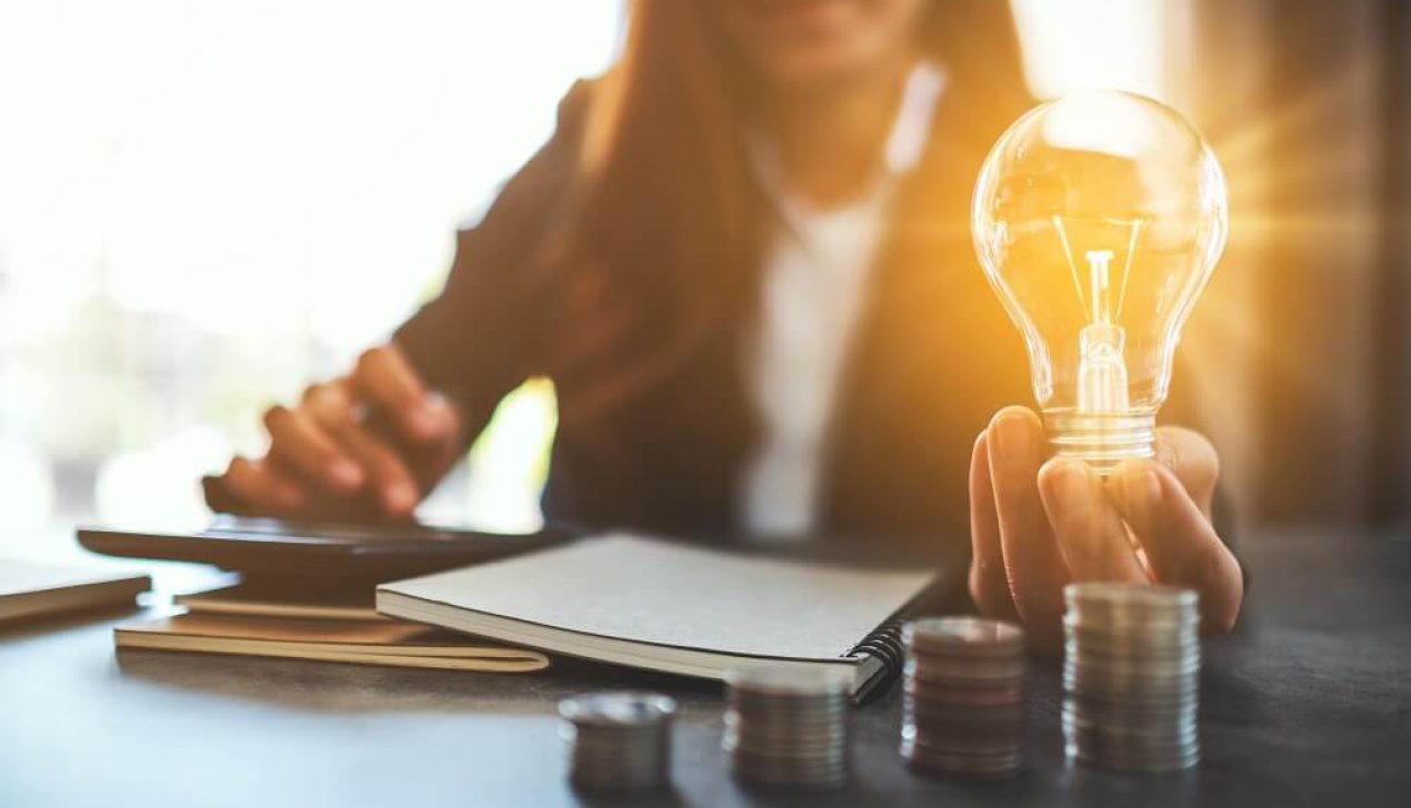 Businesswoman holding a lightbulb with coins stack on table, sav Businesswoman holding a lightbulb with coins stack on table, saving energy and money concept