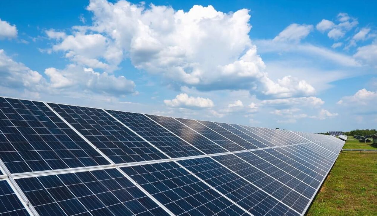 A row of solar panels in a field with clouds and a blue sky. Green energy production. A row of solar panels in a field with clouds and a blue sky. Green energy production