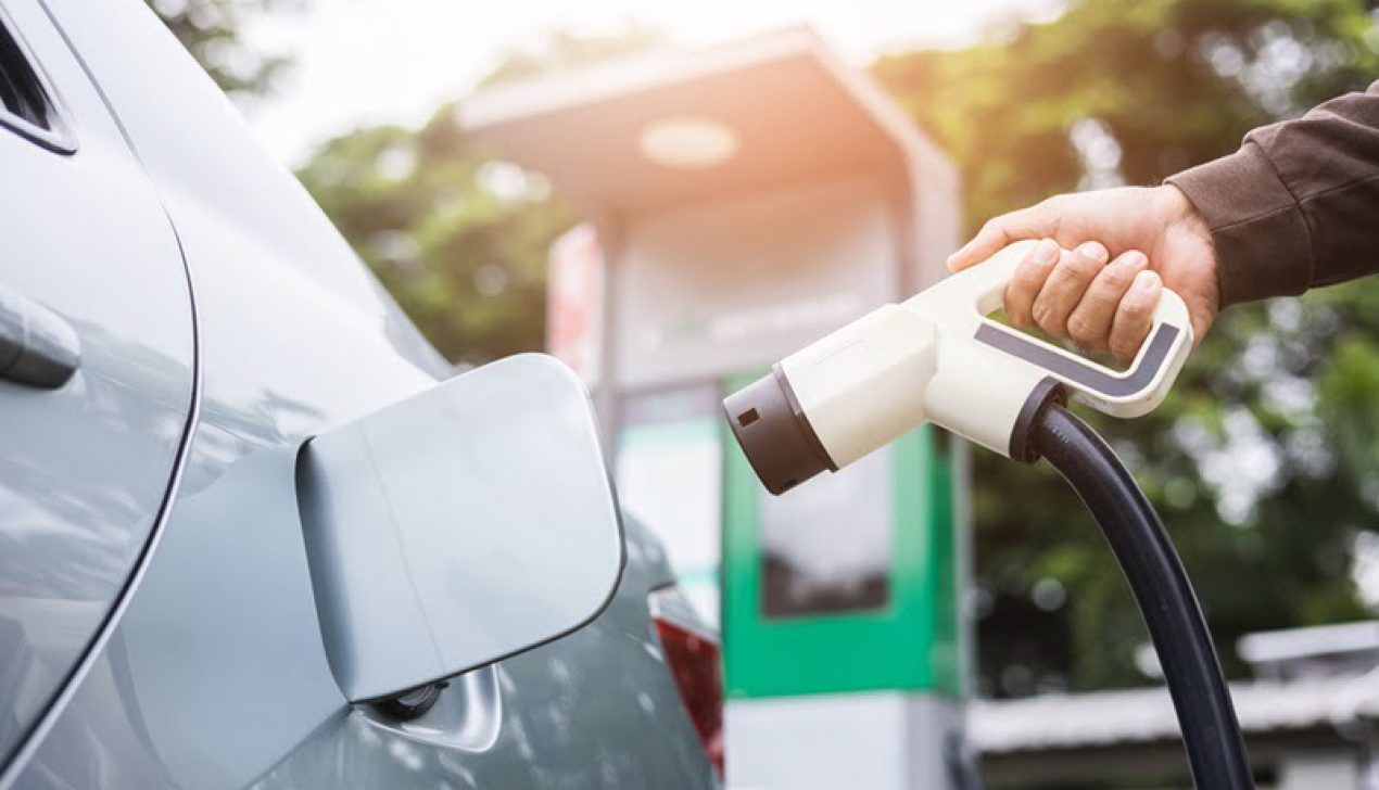 Ev car Electric car charging on parking lot. Male hand holding p Ev car Electric car charging on parking lot. Male hand holding power cable supply plugged at Electric car charging station. Eco-friendly alternative energy. Future technology battery vehicle.
