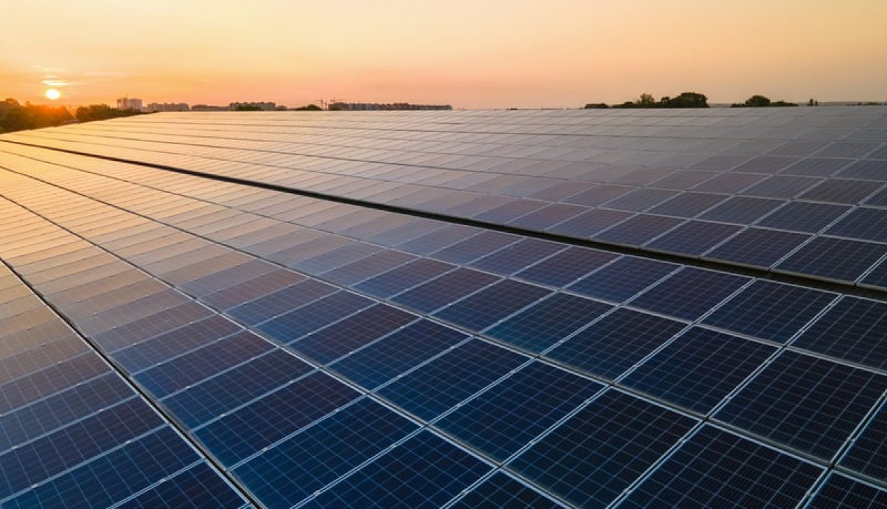 Blue photovoltaic solar panels mounted on building roof for producing clean ecological electricity at sunset. Production of renewable energy concept Blue photovoltaic solar panels mounted on building roof for producing clean ecological electricity at sunset. Production of renewable energy concept.